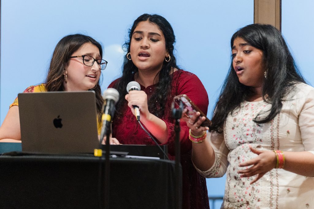 Three students sing into microphones.