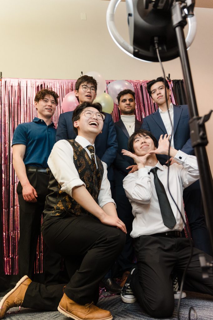 A group of 6 students pose for a selfie in front of a photo booth.