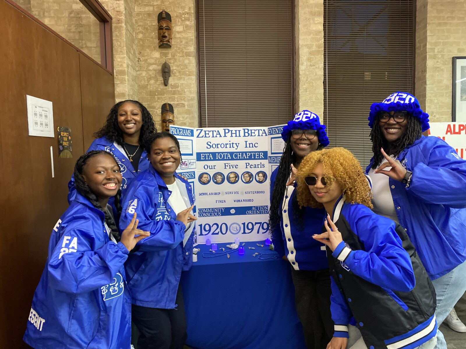 6 students in bright blue jackets posing in front of org poster.